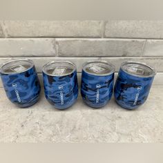 four cans of soda sitting next to each other on a marble countertop in front of a white brick wall