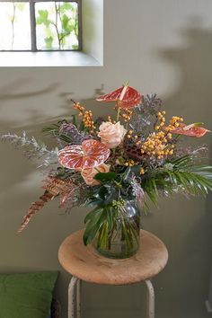 a vase filled with lots of flowers on top of a wooden table next to a window