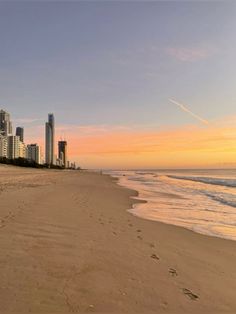 a beach with buildings in the background and footprints in the sand on the foreground