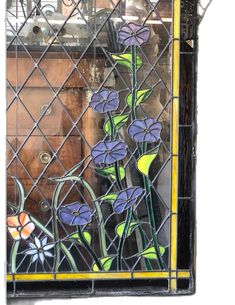 a stained glass window with purple flowers and green leaves on the outside, in front of a wooden cabinet