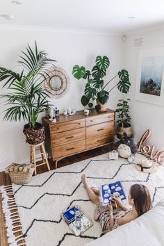 a woman laying on top of a bed next to a dresser and potted plant