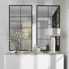 a white dresser with mirrors and vases on it next to a lamp in a room