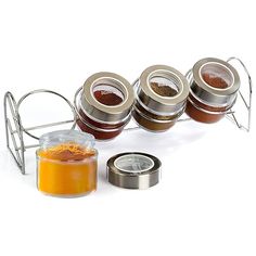 four spice jars with lids and spices in them on a white surface next to a metal rack