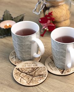 two cups of tea sit on coasters next to cookies