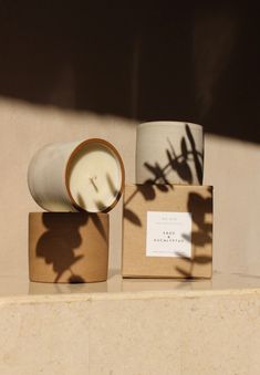 a candle and some boxes on a shelf with the shadow of a plant behind it