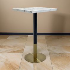 a white marble table with a black metal base and gold colored legs on a tiled floor