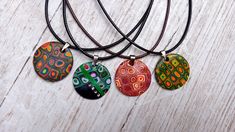 four necklaces with different designs on them sitting on a wooden surface, one is multicolored and the other has black cord