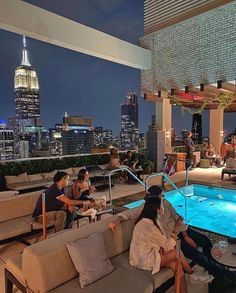 people sitting on couches in front of an outdoor swimming pool at night with the city skyline behind them