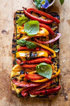 grilled vegetables with basil and peppers on a wooden board next to a potted plant