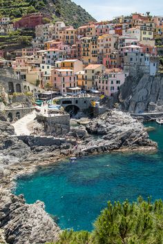 the village is on top of a cliff overlooking the ocean and beach below it, with people swimming in the blue water