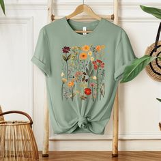 an unisex t - shirt with flowers and leaves on the front, tied to a hanger