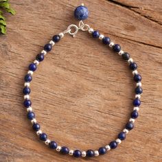 a blue beaded bracelet with silver beads on top of a wooden table next to a plant