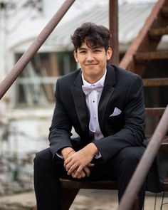 a young man in a tuxedo sitting on a bench smiling at the camera