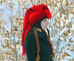 a woman wearing a red hat with braids in front of snow covered trees and bushes