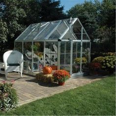 a white chair sitting on top of a wooden floor next to a green house filled with flowers