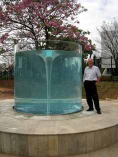 a man standing in front of a large glass vase with water pouring out of it