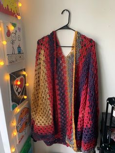 a crocheted sweater hanging on a wall next to a coat rack with lights