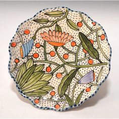 a decorative plate with flowers and leaves painted on the front, sitting on a white surface