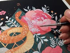 someone is painting flowers and a snake on a piece of paper