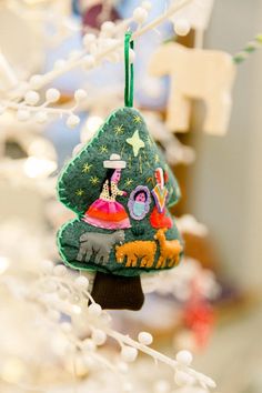 an ornament hanging from a christmas tree decorated with felt animals and other decorations