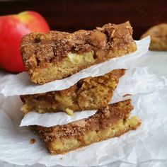 three pieces of apple pie sitting on top of white paper next to an orange and red apple