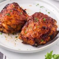 two pieces of chicken on a white plate with parsley sprinkled around it