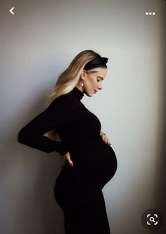 a pregnant woman in a black dress poses for the camera with her hands on her hips