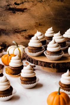 there are many cupcakes on the table with white frosting and pumpkins