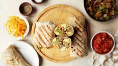 some food is laying out on a wooden plate next to bowls and plates with condiments