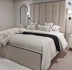 a bed with white sheets and pillows in a bedroom next to a mirror on the wall