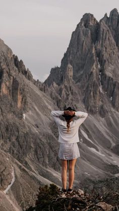 a woman standing on top of a mountain with her hands behind her head looking at the mountains