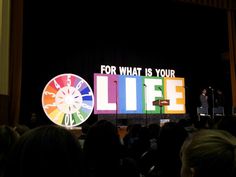 a man standing on top of a stage next to a giant wheel of fortune sign