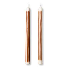 two candles sitting next to each other on top of a white surface with brown trim