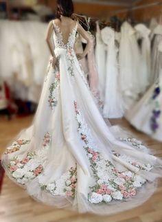 a woman standing in front of a rack of wedding gowns with flowers on them