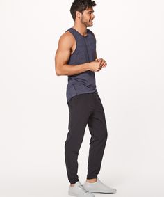 a man standing in front of a white background wearing black pants and a tank top