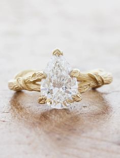 a pear shaped diamond sits on top of a wooden surface, with leaves around it