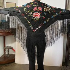 DETAILS A small, vintage traditional Flamenco dancer's black shawl or mantoncillo pico with a floral embroidery design and long fringe.  COLOR(S) Multi-color on black ground  PLACE OF ORIGIN Spain | Europe  DATE 20th century  DIMENSIONS Width 63 Depth 63 inches Without fringe: Width 36 Depth 36 inches Black Bohemian Shawl For Spring, Black Folk Style Shawl For Festival, Vintage Embroidered Shawl For Spring, Traditional Embroidered Shawl For Spring, Black Fringed Shawl For Festival, Traditional Black Shawl With Floral Embroidery, Black Shawl With Traditional Patterns For Festivals, Black Embroidered Bohemian Shawl, Black Bohemian Shawl With Embroidered Border