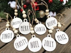 six christmas tags with words on them sitting next to a pine tree and ornaments in the background