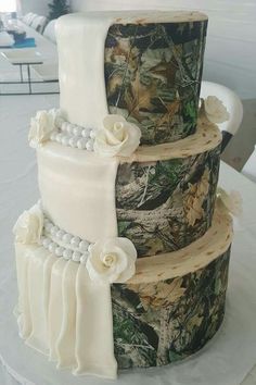 three tiered camouflage wedding cake with white flowers and pearls on the top, decorated with ribbon