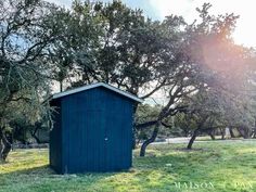 a blue outhouse sitting in the middle of a green field next to some trees