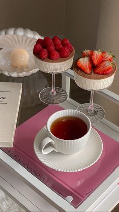 two desserts with strawberries on them and a cup of tea sit on a tray