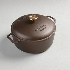 a brown casserole on a white surface with a gold lid and handle that says lunch over it