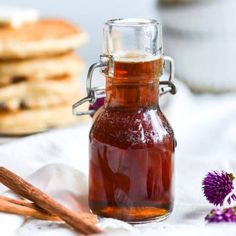 a glass bottle filled with syrup next to some cinnamon sticks