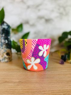 a colorful cup sitting on top of a wooden table next to a potted plant