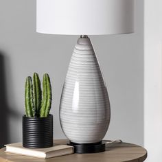 a white vase sitting on top of a table next to a green cactus in a black pot