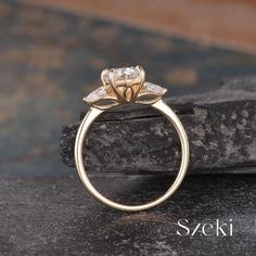 a gold ring with a flower design on the front and side, sitting on top of a rock