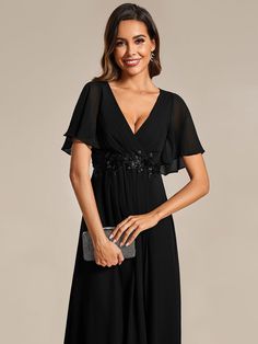 a woman wearing a black dress with sheer sleeves and an embellishment on the waist