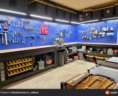 there are many tools hanging on the wall in this garage area with blue tiles and yellow bins