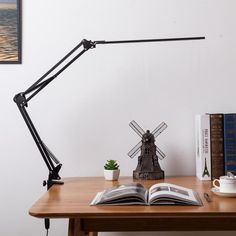 an open book sitting on top of a wooden desk next to a lamp and books