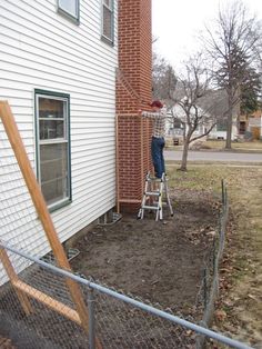 a man standing on a ladder in front of a brick building while painting the side of a house